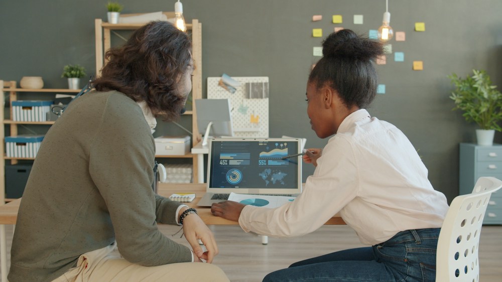 Two colleagues reviewing data on a laptop.